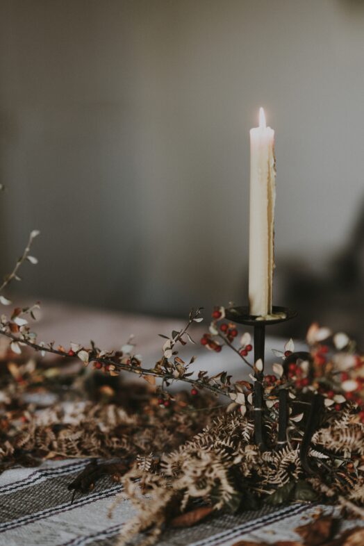 Ett tänt ljus i en ljusstake omgiven av torkade blommor och växter.