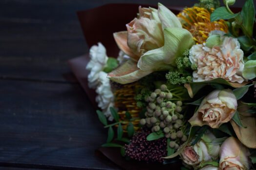 En bukett med olika blommor, inklusive vita och gula blommor, mot en mörk bakgrund.